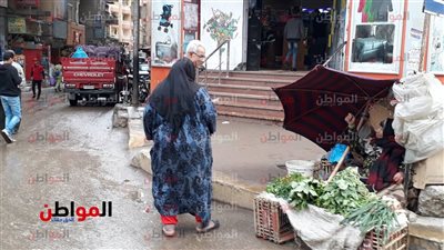 صور | بالشمسية والإيشارب .. أمطار شارع فيصل تعزز الأمل لدى بائعة الخضروات